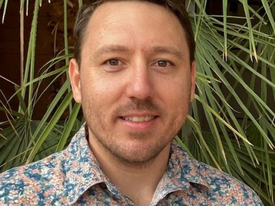 Headshot of man wearing light blue and pink floral shirt smiling at the camera