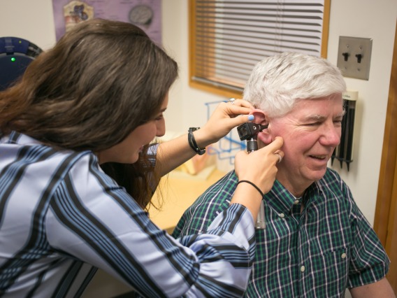 A graduate clinician uses an otoscope to look into an adult client's ear