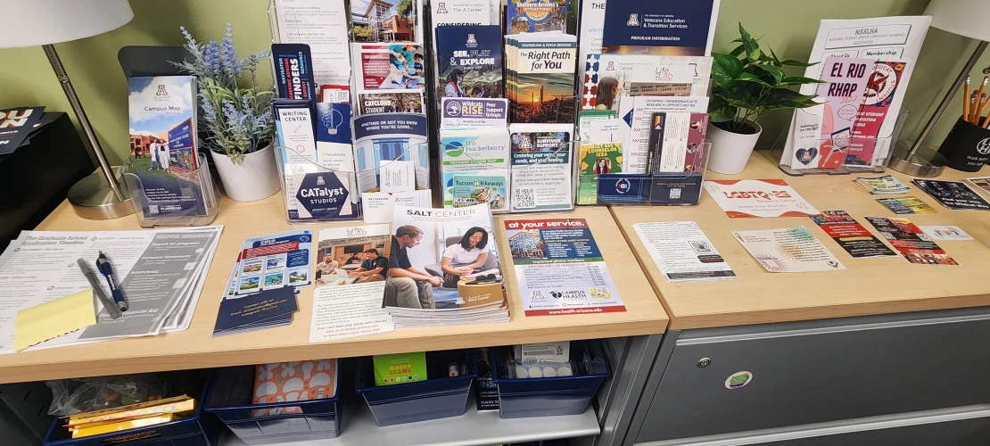 desk covered in flyers and pamphlets for UA-related or Tucson-related resources