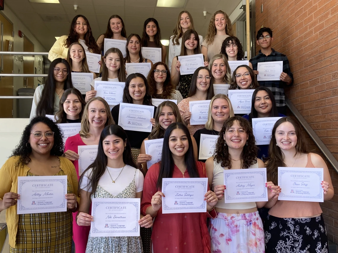 Image of about 25 college students standing on a stairway holding certificates in front of them and all smiling at the camera.