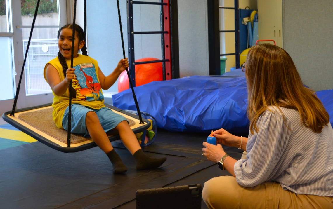 young patient on a swing with a clinician in The Delaney Schnell Speech and Language Gym