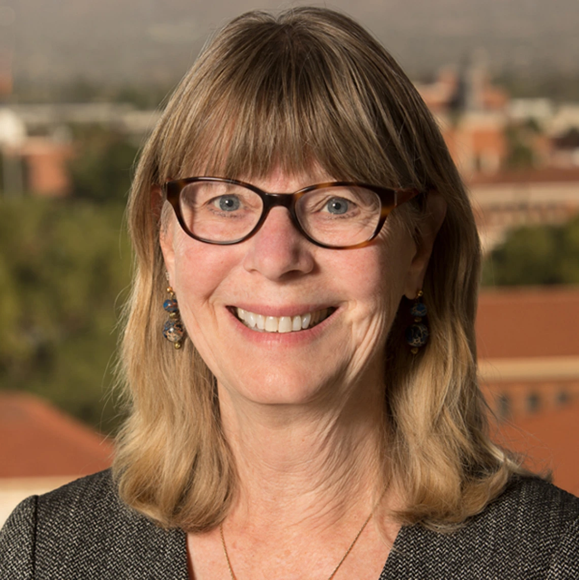 Headshot of woman with medium brown shoulder length hair and glasses wearing a dark shirt smiling at camera