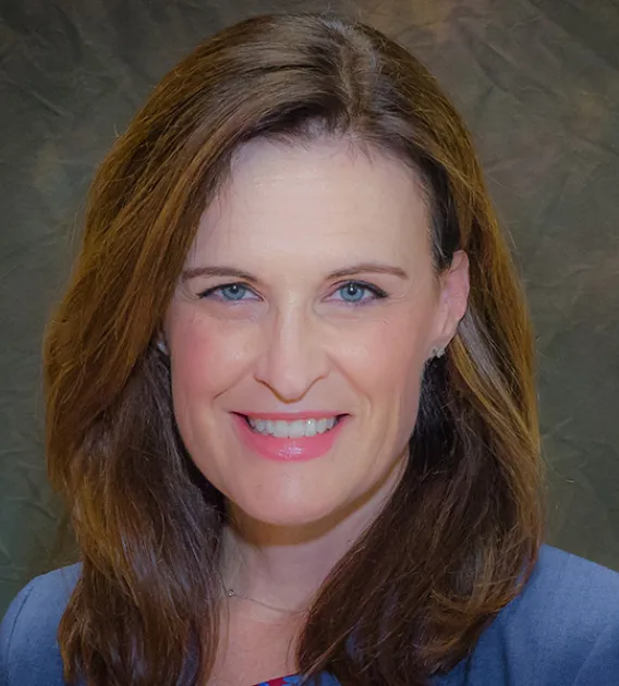 Headshot of woman with long brown hair wearing a light blue blazer smiling at the camera.