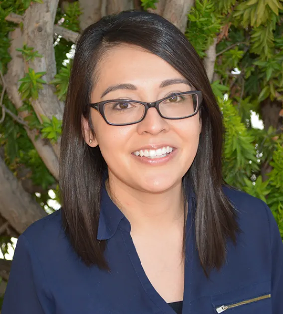 Headshot of woman with dark shoulder length hair parted on the side wearing glasses and a blue blouse smiling at the camera.