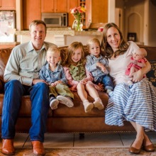 Parents with four children sitting on couch smiling at camera.